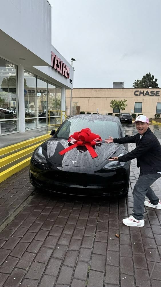 Person posing beside a black Tesla with a red bow