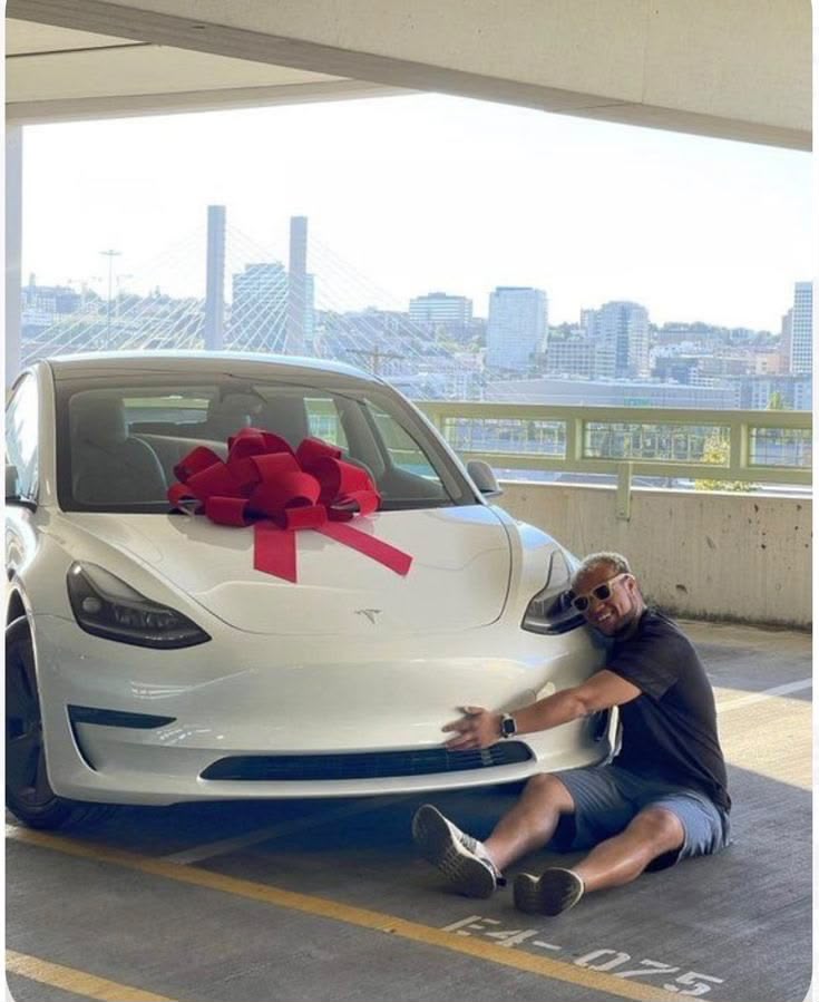 Person celebrating beside a white Tesla with a red bow